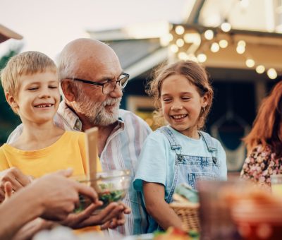 Tre generationer nyder et måltid sammen i haven – symbol på langsigtet opsparing og pensionsinvestering med tryghed