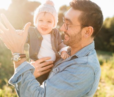 Far løfter smilende baby i solen udendørs