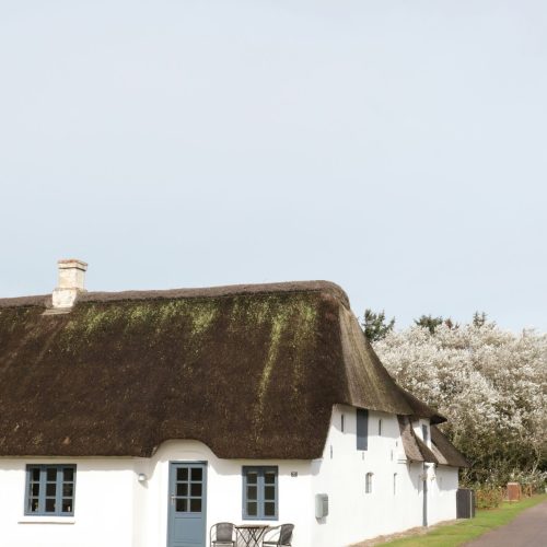 Hvidt stråtækt hus ved landevej i dansk landskab